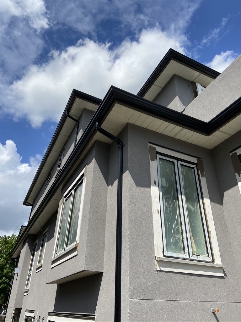 Black seamless gutter installed on a grey stucco home