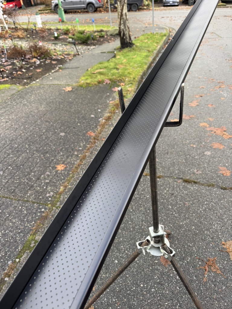 Black perforated gutter guard material staged for installation