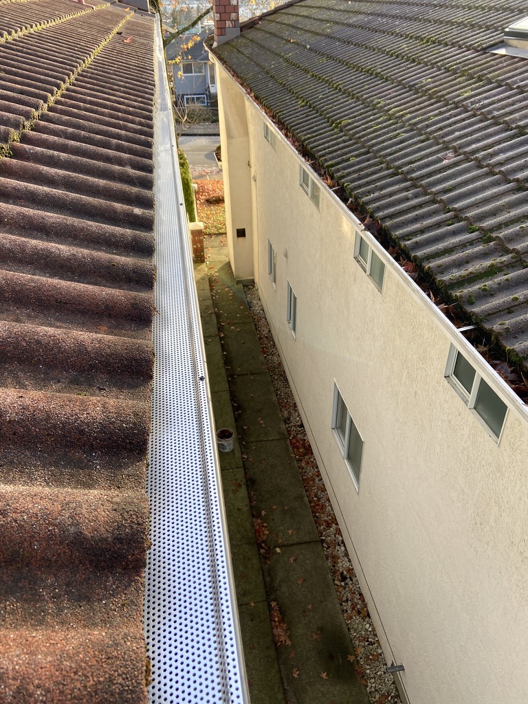 White gutter guard installed along a tile-style roof edge