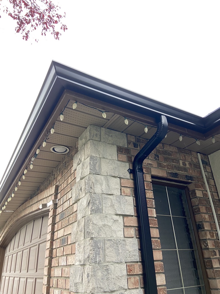 Finished black downspout and seamless gutter on a brick home corner